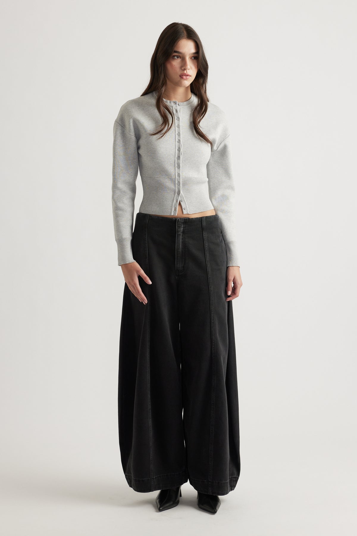 Woman wearing a light grey cinched knit cardigan paired with wide-leg black jeans and black pointed boots
