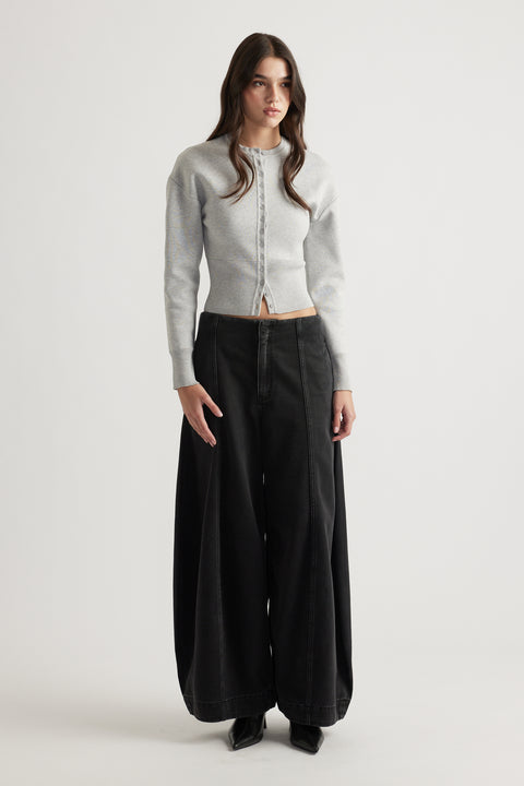 Woman wearing a light grey cinched knit cardigan paired with wide-leg black jeans and black pointed boots