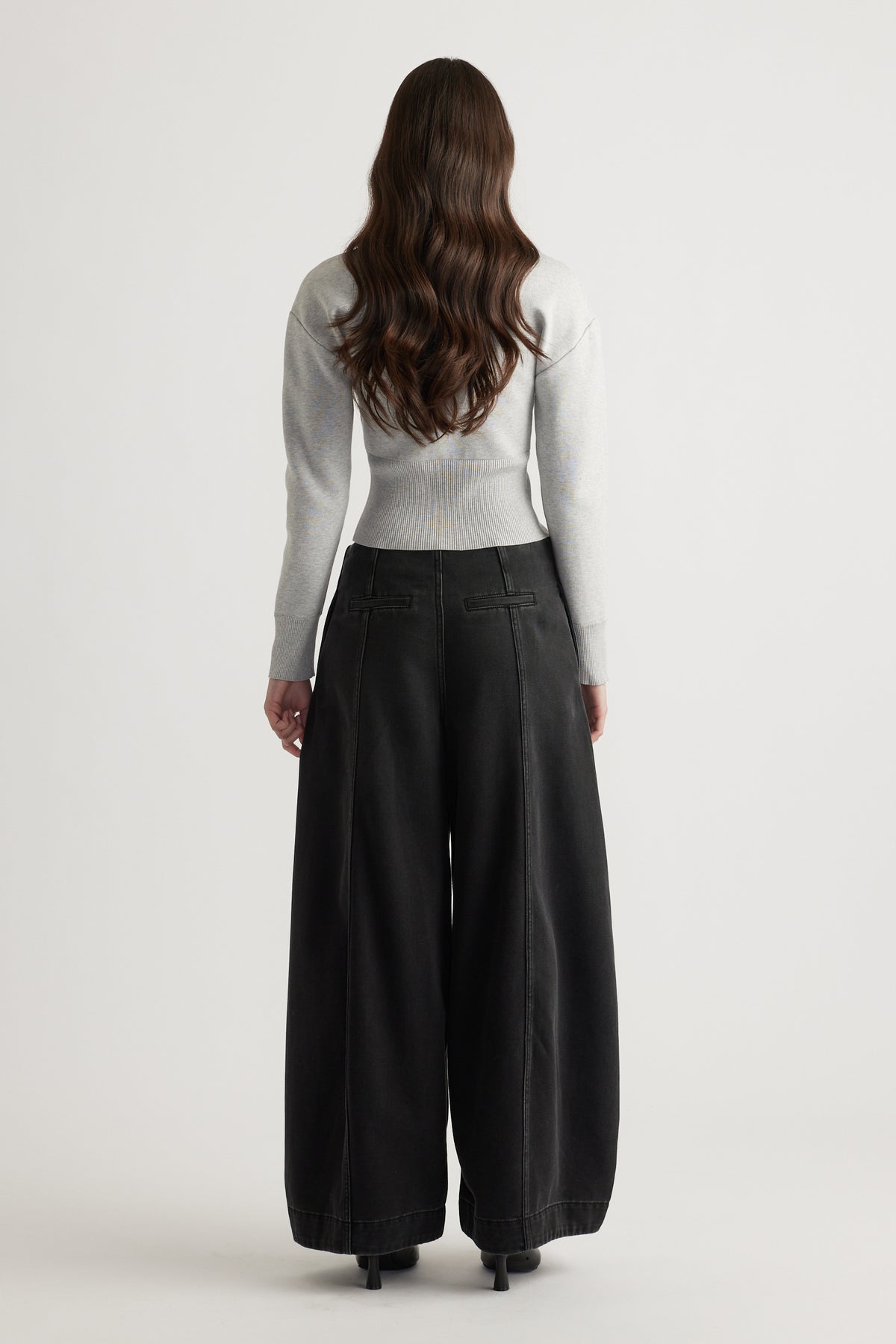 Back view of woman wearing a light grey fitted knit cardigan paired with wide-leg black pants and heels.
