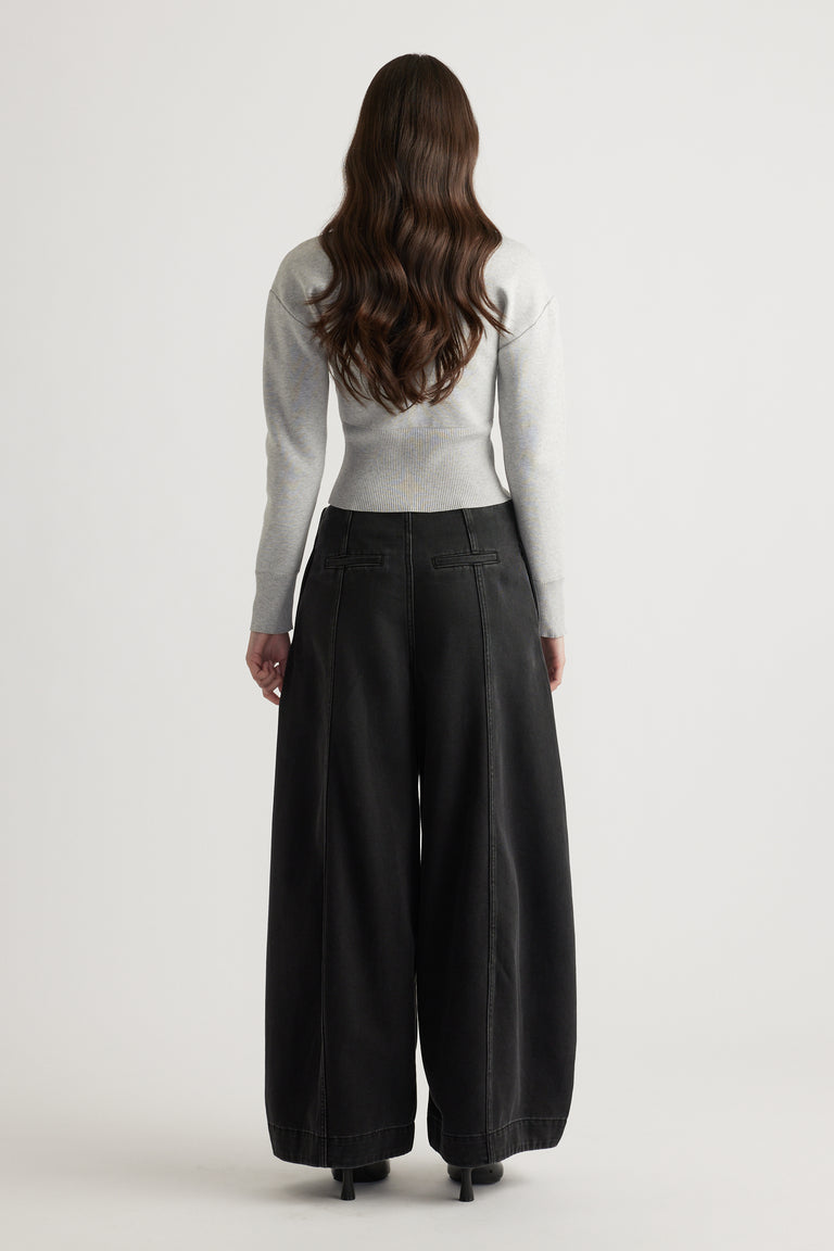 Back view of woman wearing a light grey fitted knit cardigan paired with wide-leg black pants and heels.