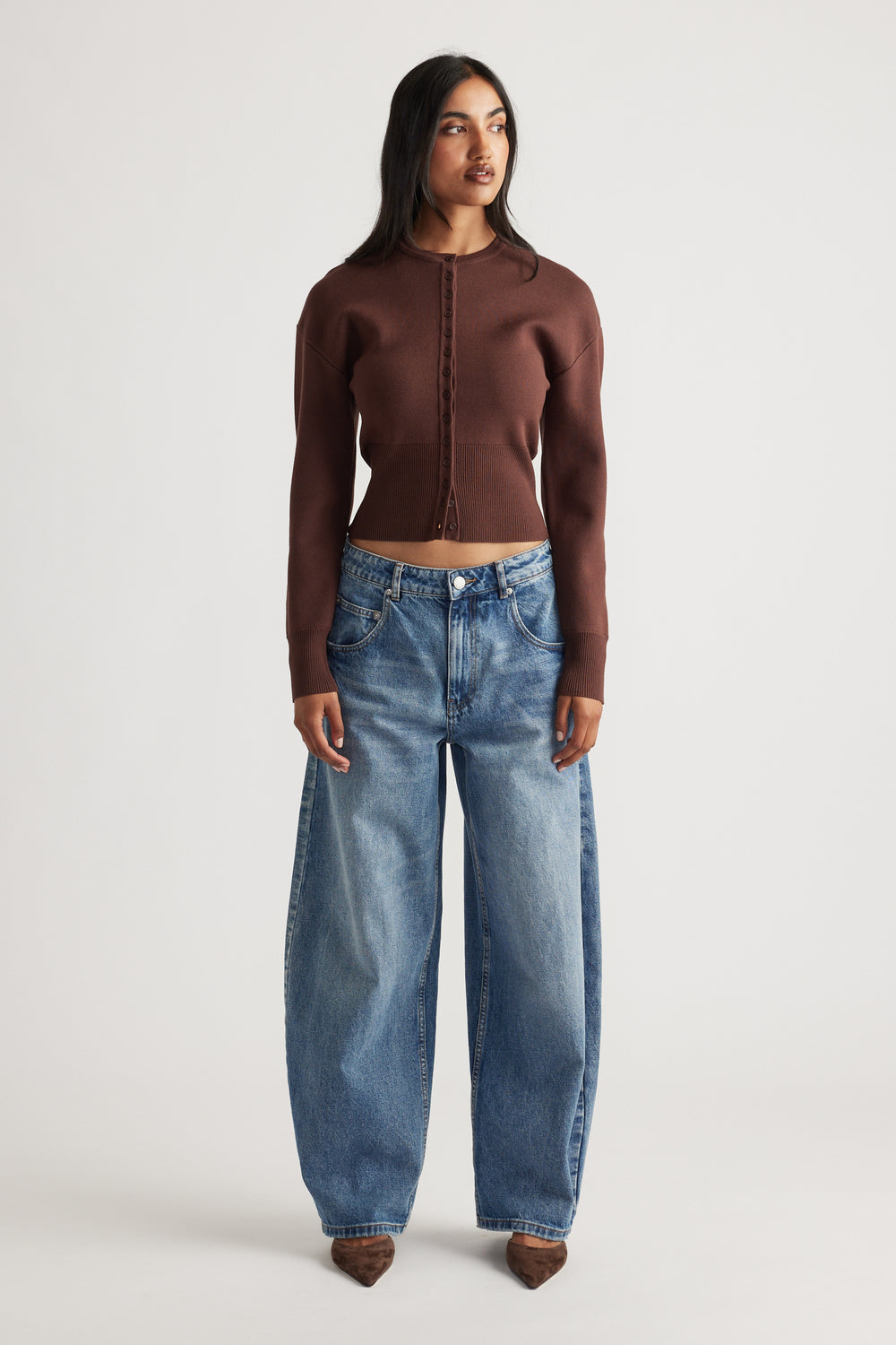 Woman wearing a fitted rich mocha cardigan with cinched waist paired with relaxed wide-leg blue denim jeans and pointed shoes