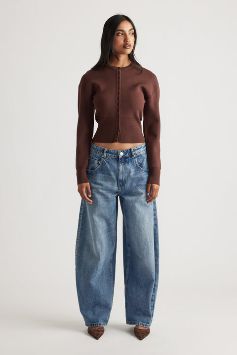 Woman wearing a fitted rich mocha cardigan with cinched waist paired with relaxed wide-leg blue denim jeans and pointed shoes