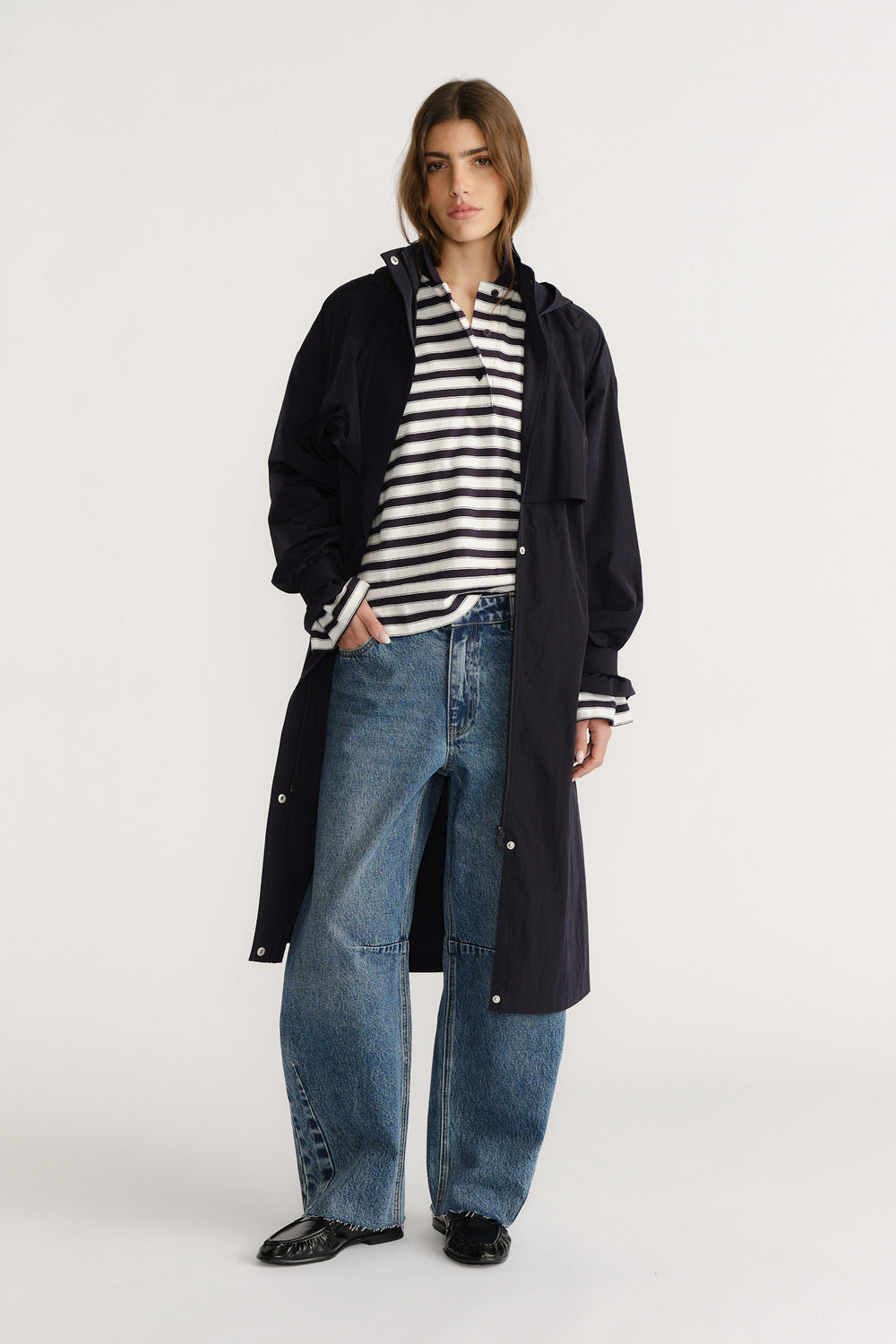 Woman wearing a navy longline coat over a striped rugby shirt and relaxed wide-leg jeans with black flats.