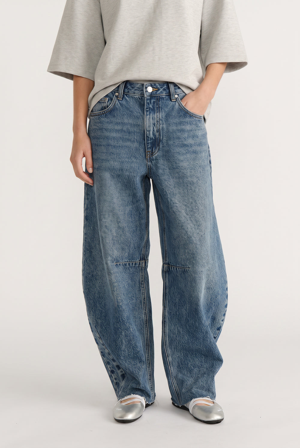 Woman wearing high-rise wide-leg denim jeans with curved silhouette paired with silver ballet flats and grey top