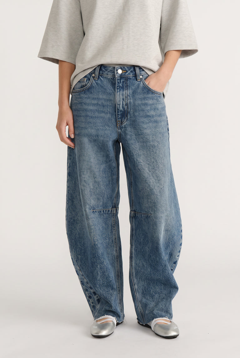 Woman wearing high-rise wide-leg denim jeans with curved silhouette paired with silver ballet flats and grey top