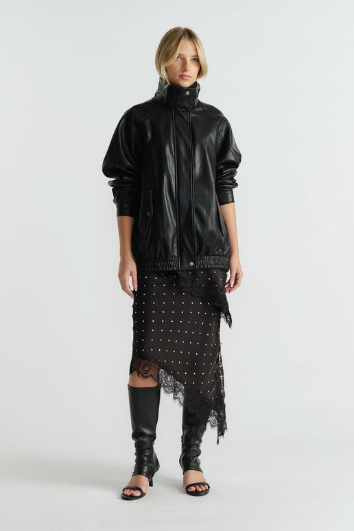 Woman wearing black leather jacket over midi slip skirt with lace trim and asymmetric hem paired with knee-high boots