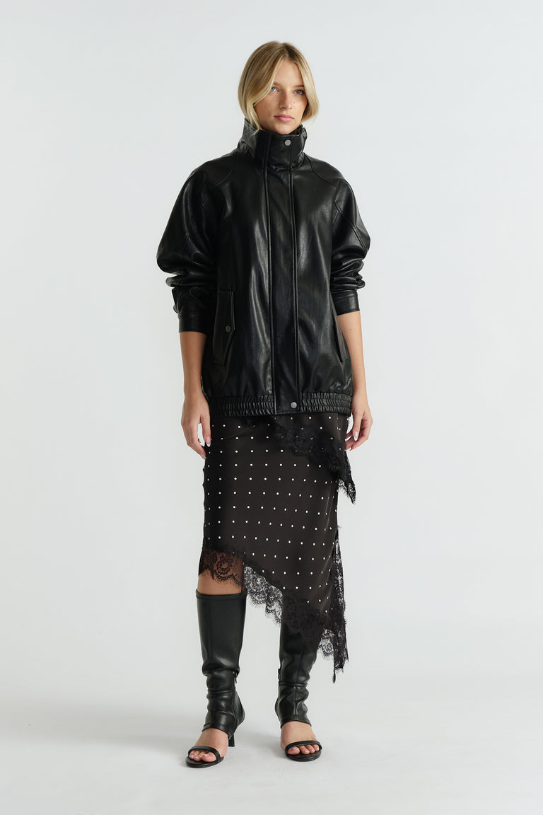 Woman wearing black leather jacket over midi slip skirt with lace trim and asymmetric hem paired with knee-high boots