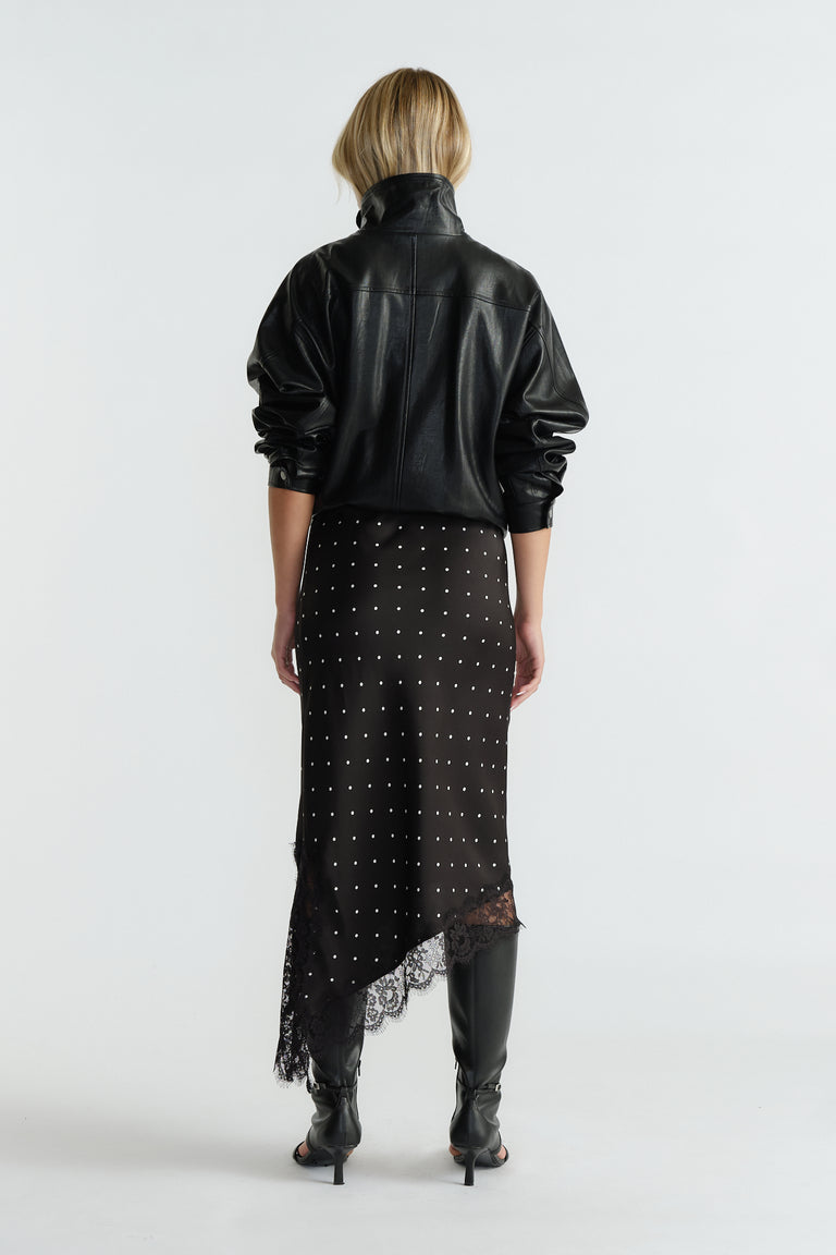 Rear view of woman wearing black asymmetric hem midi skirt with lace trim and studded detail paired with black jacket