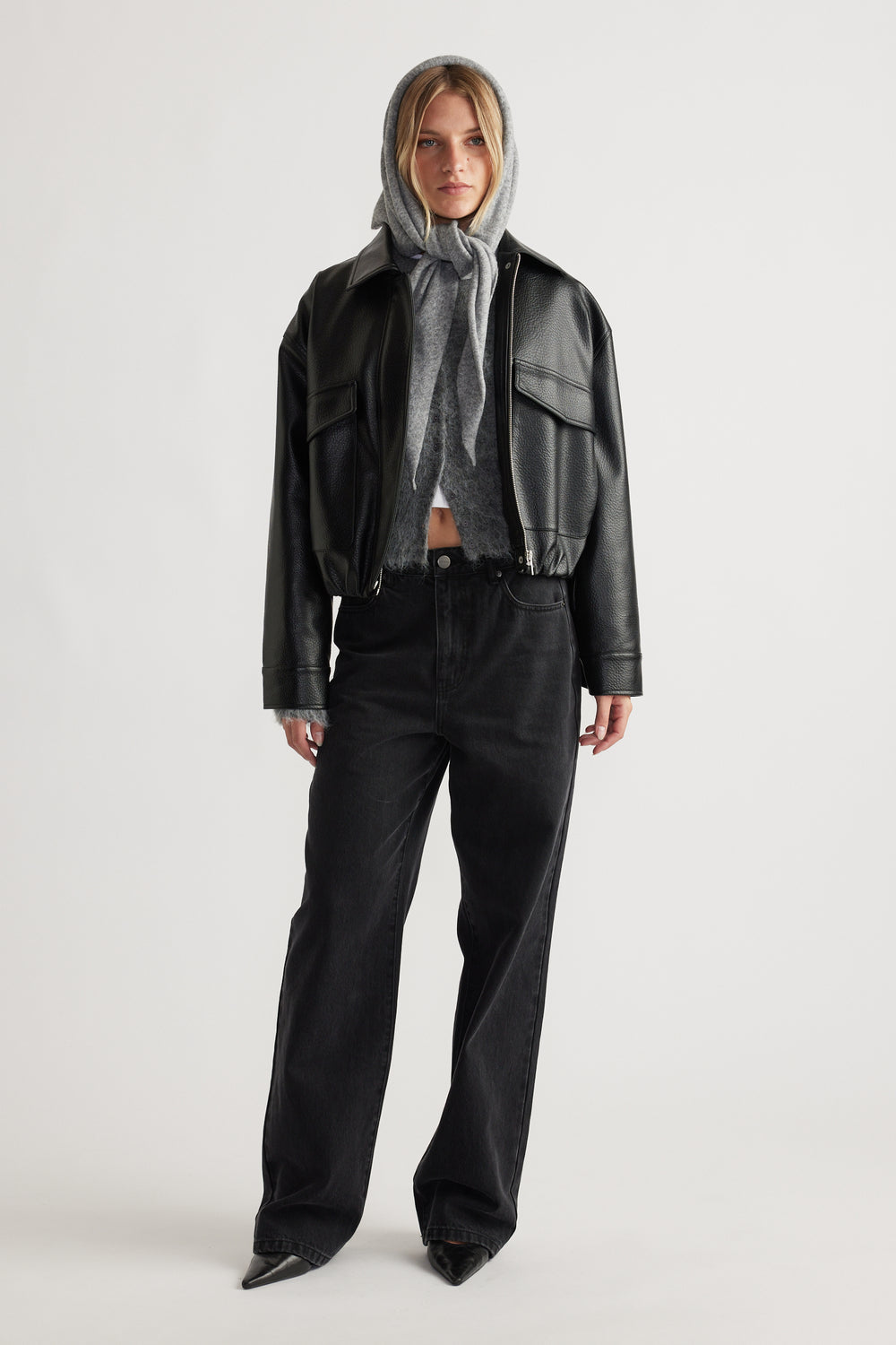 Front view of woman wearing Heather Triangle Scarf in grey layered under black leather jacket and black wide-leg denim jeans