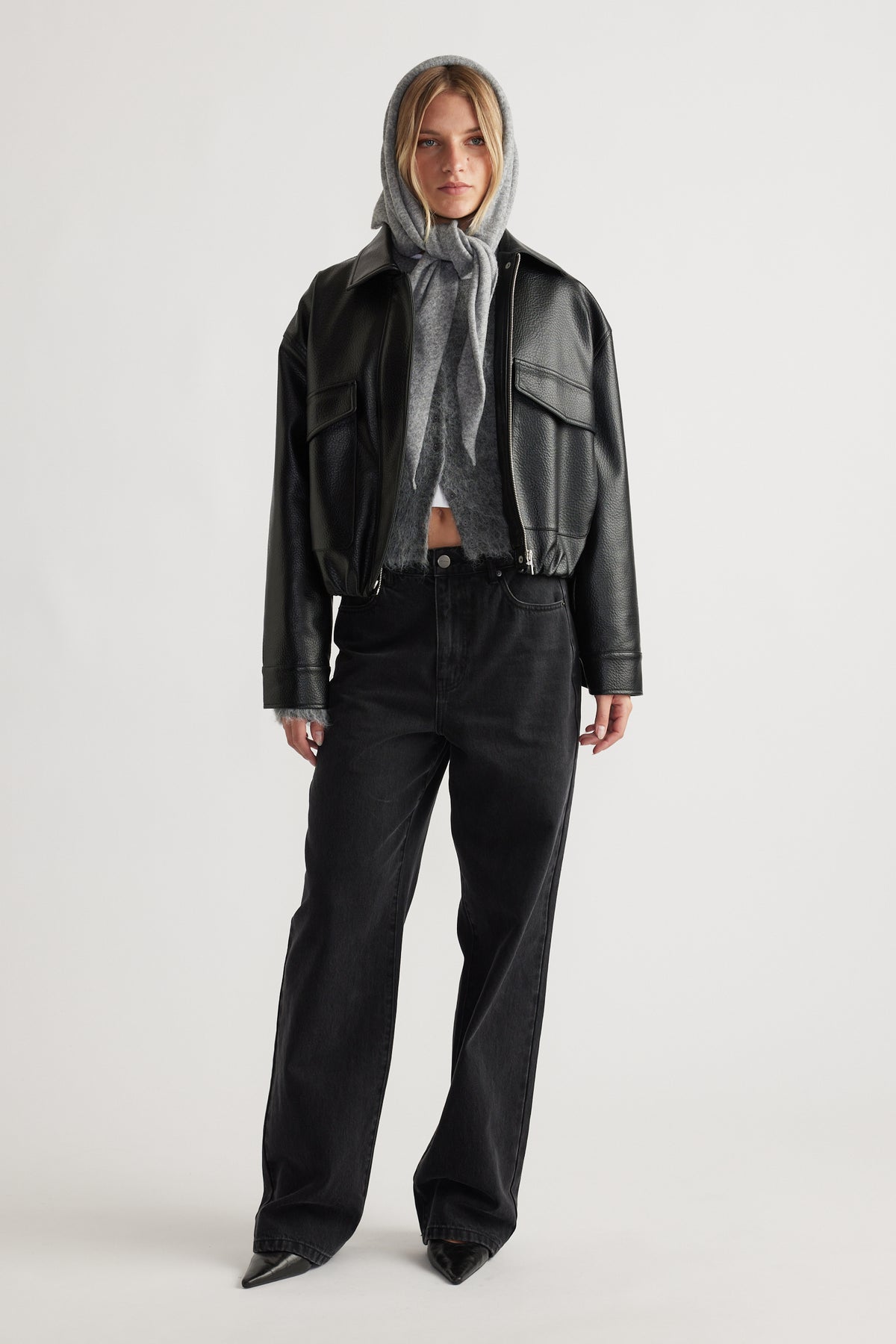 Front view of woman wearing Heather Triangle Scarf in grey layered under black leather jacket and black wide-leg denim jeans