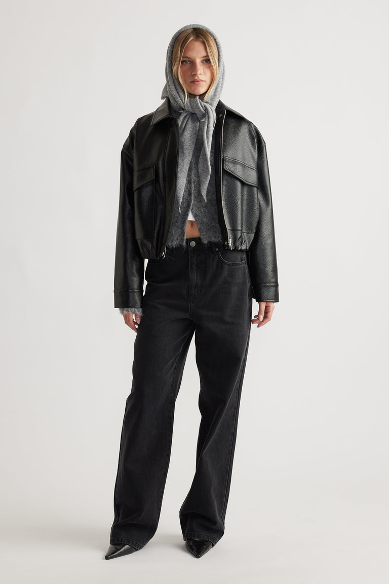 Front view of woman wearing Heather Triangle Scarf in grey layered under black leather jacket and black wide-leg denim jeans