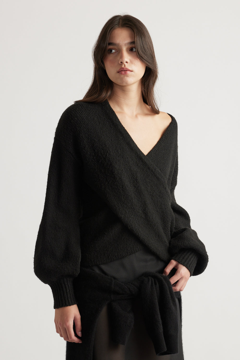Woman wearing a soft black crossover knit jumper with balloon sleeves and a relaxed fit, styled casually with a tied sweater.