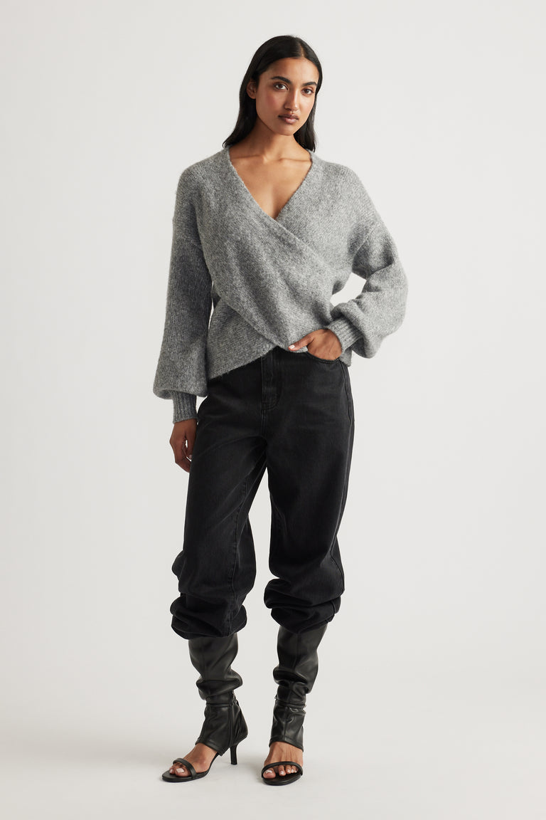 Woman wearing a soft grey crossover jumper styled with relaxed black jeans and black heeled boots for an easy chic look