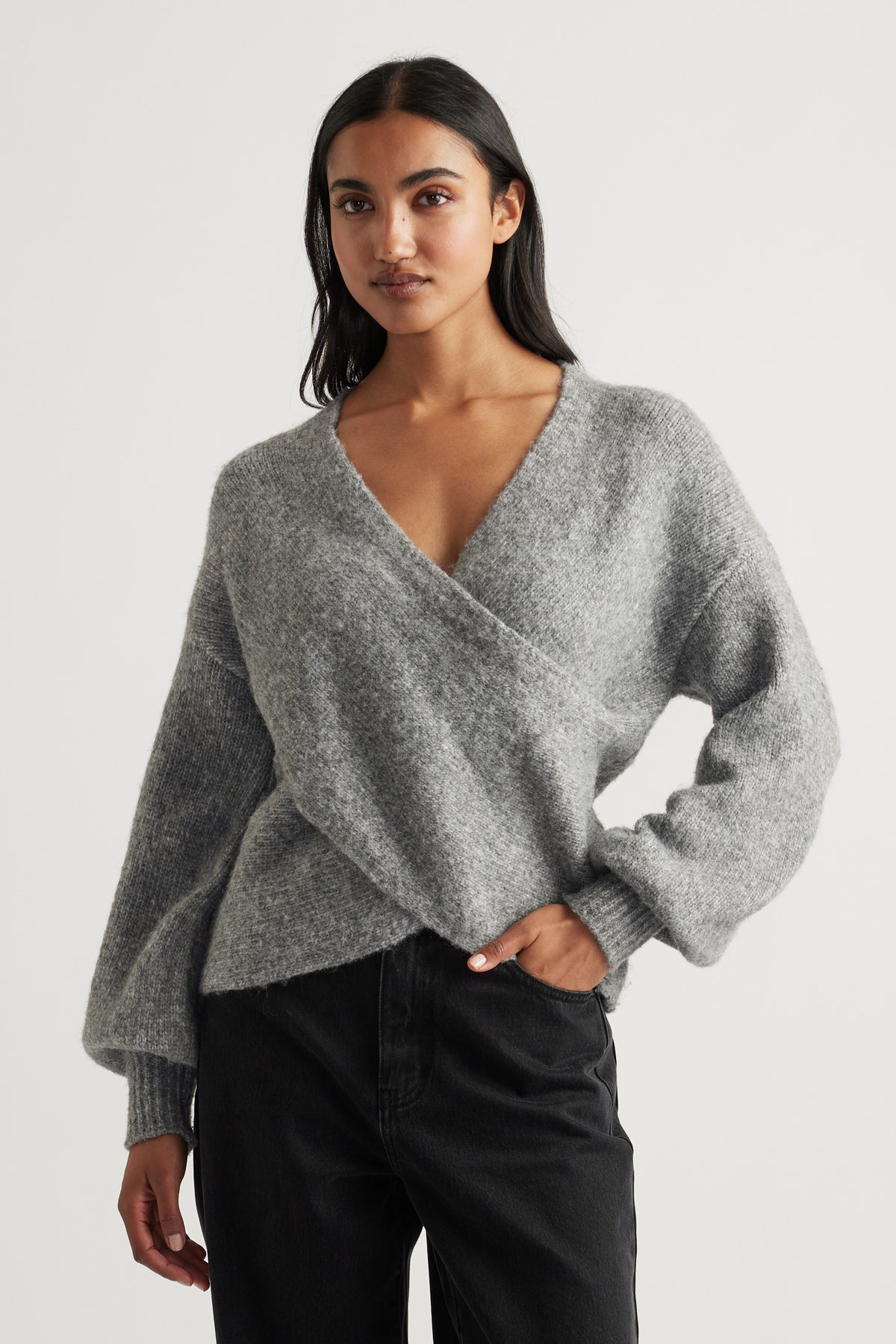 Woman wearing a soft mid-grey crossover knit jumper paired with relaxed black jeans for a cozy, casual look