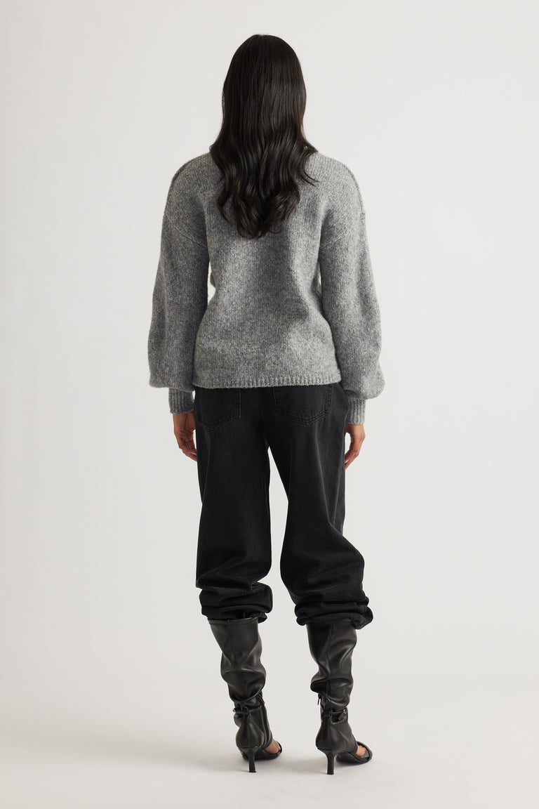 Woman seen from behind wearing a soft grey jumper with puff sleeves, black relaxed-fit pants, and slouchy heeled boots
