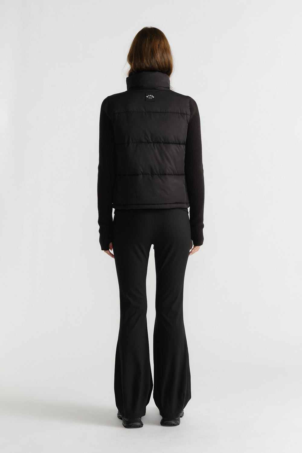 Back view of woman wearing a black knit puffer jacket with fitted long sleeves and flared black pants for a sleek style.