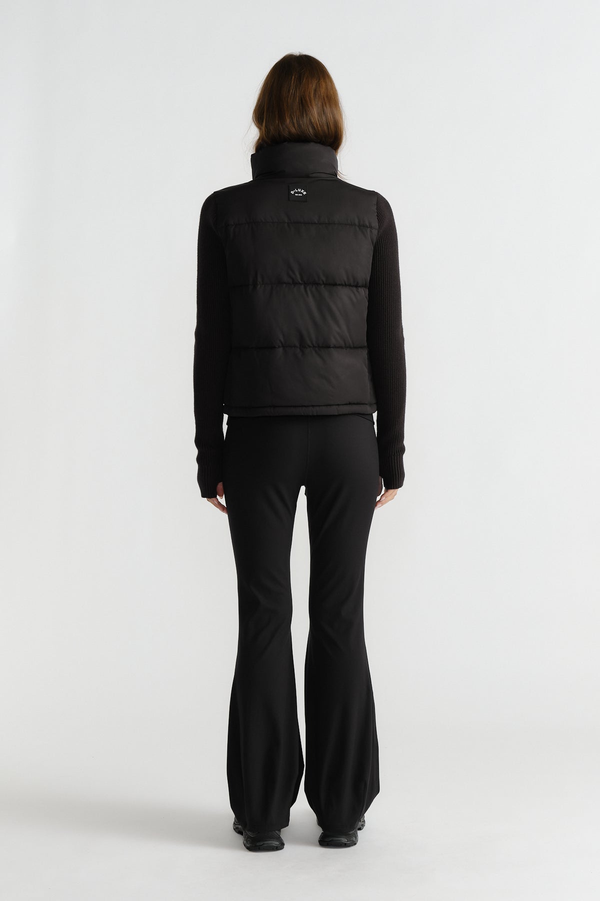 Back view of woman wearing a black knit puffer jacket with fitted long sleeves and flared black pants for a sleek style.