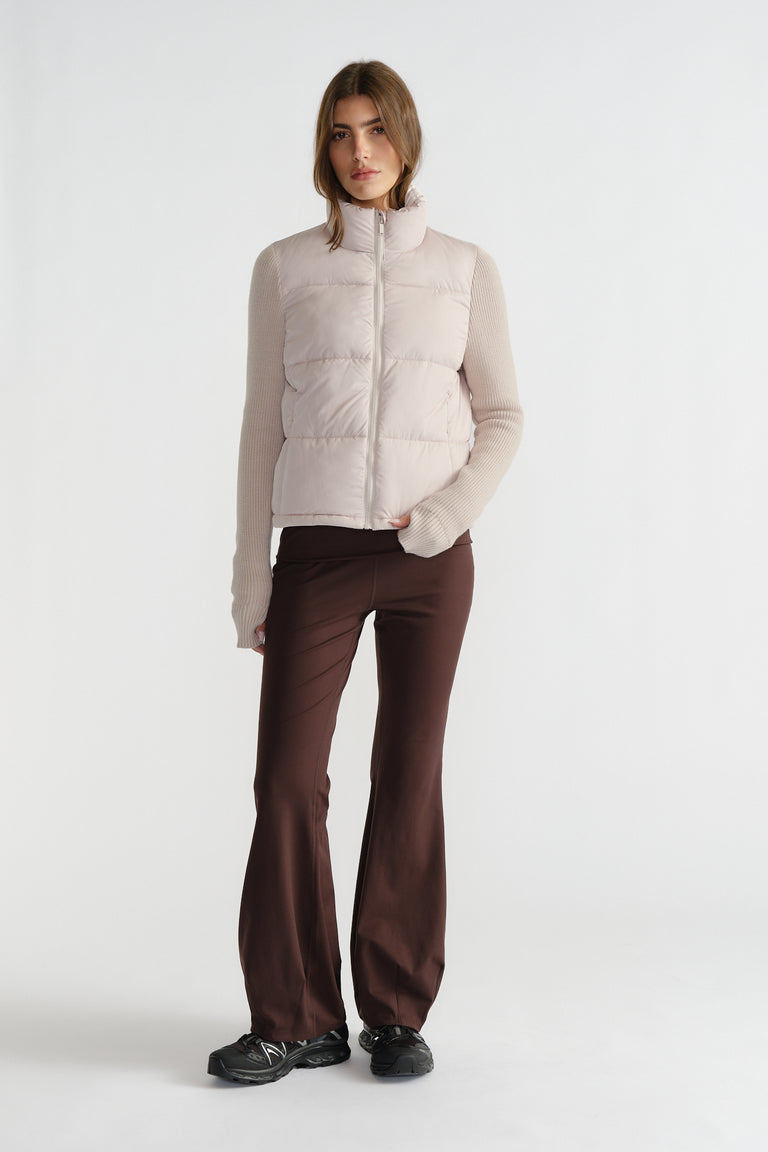 Woman wearing a light beige knit puffer jacket with ribbed sleeves paired with dark brown flared pants and black sneakers