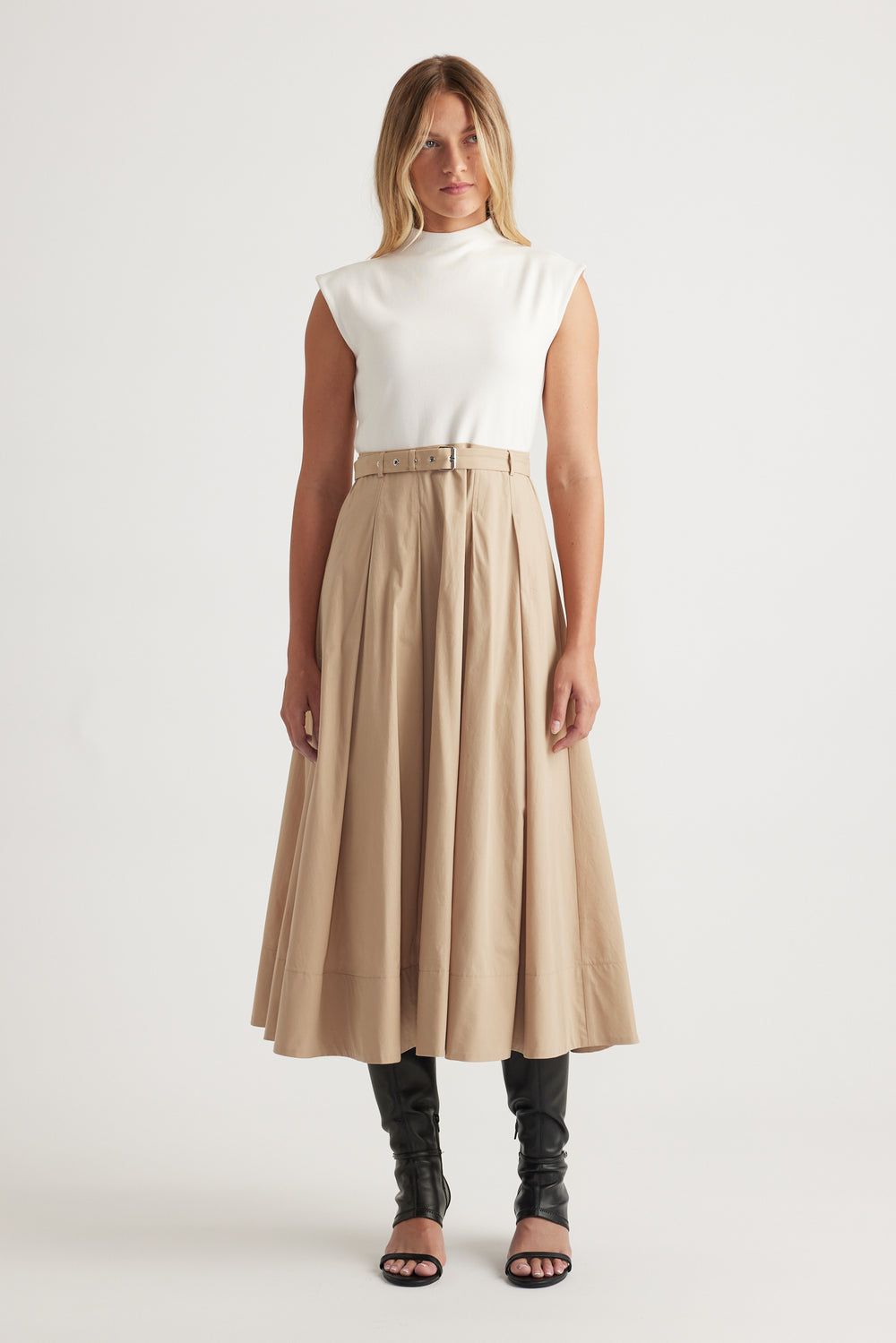 Woman wearing Stefanie Spliced Midi Dress in warm tan with belted waist, structured pleats, styled with black boots and heels