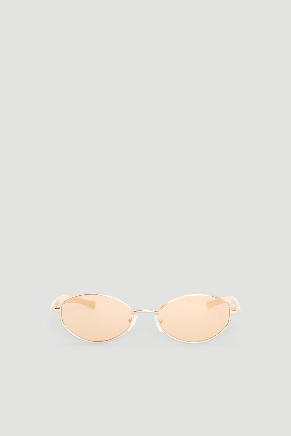 Slim oval sunglasses with gold-toned metal frames and warm beige tinted lenses for a chic, modern look.
