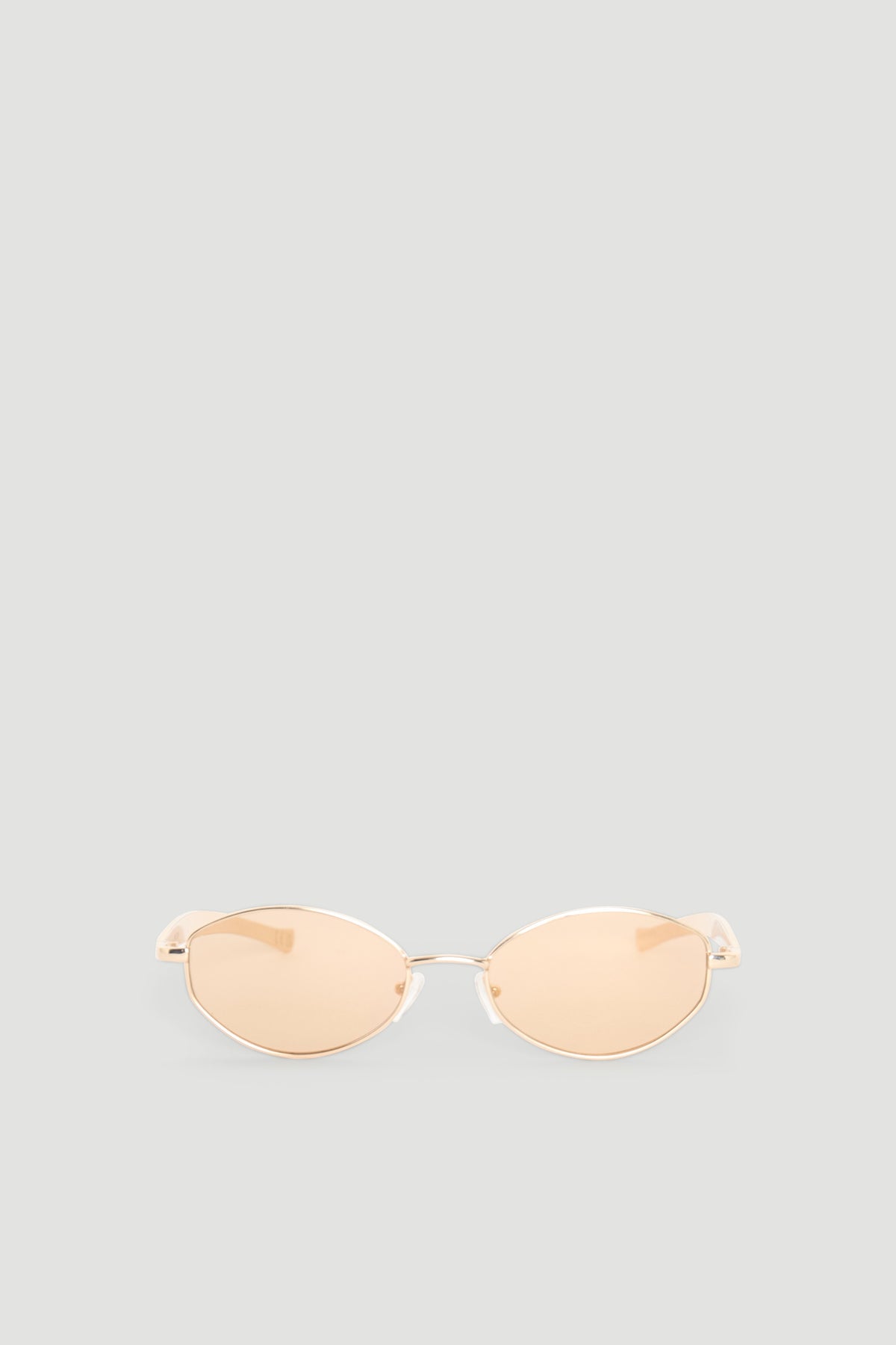 Slim oval sunglasses with gold-toned metal frames and warm beige tinted lenses for a chic, modern look.