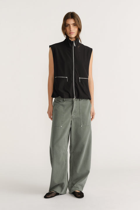 Woman wearing a sleeveless black zip-up vest with high collar paired with loose wide-leg olive green pants and black flats