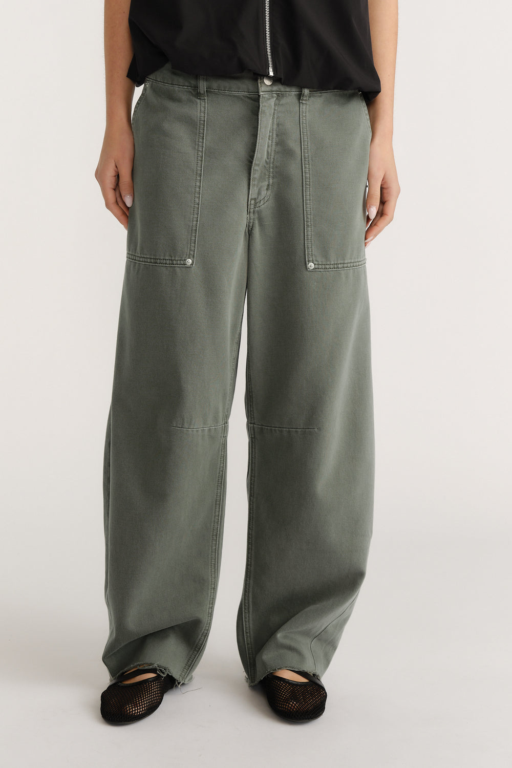 Wide-leg green jeans with exposed stitching and front pockets paired with black mesh shoes and a black top