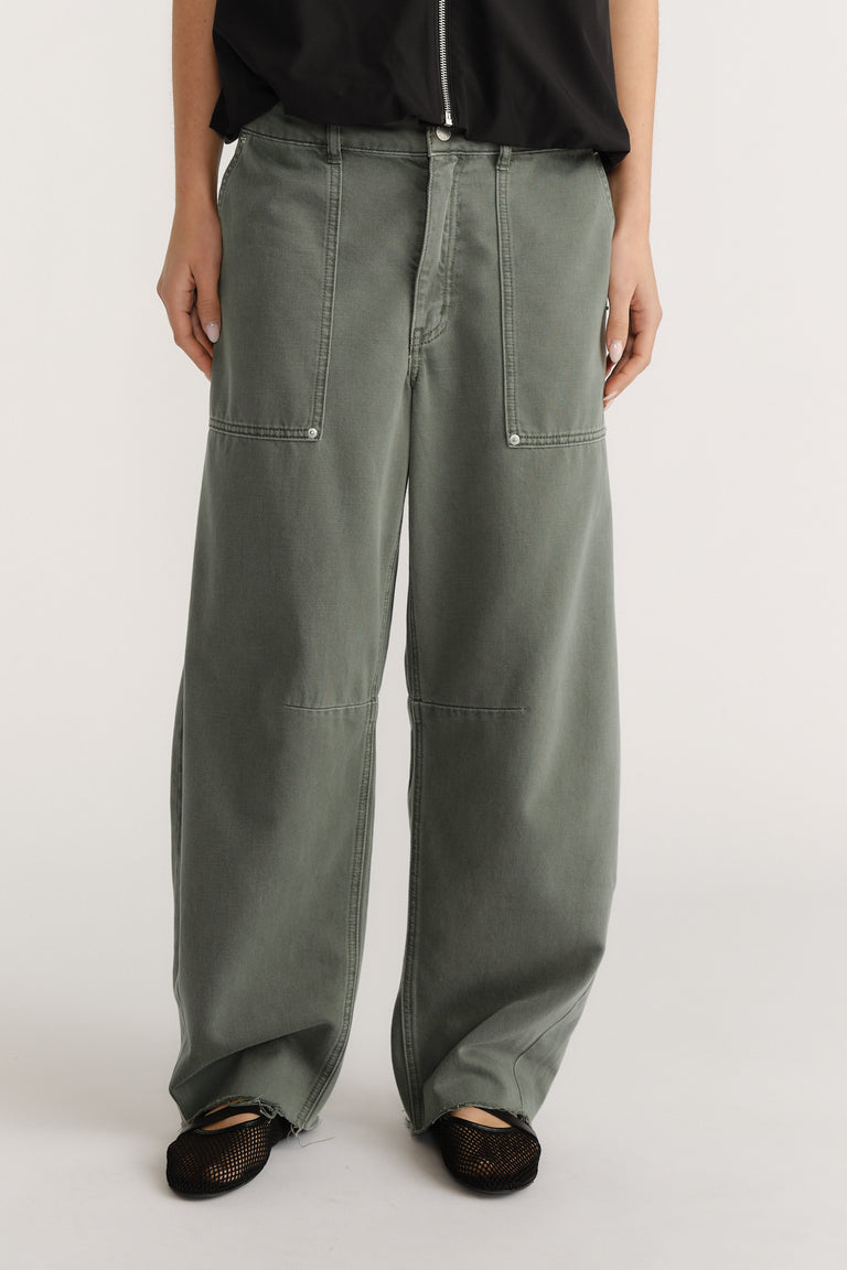 Wide-leg green jeans with exposed stitching and front pockets paired with black mesh shoes and a black top