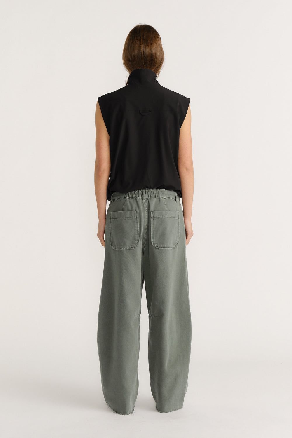Woman wearing a sleeveless black top paired with high-rise loose-fit green wide-leg pants with patch pockets at back