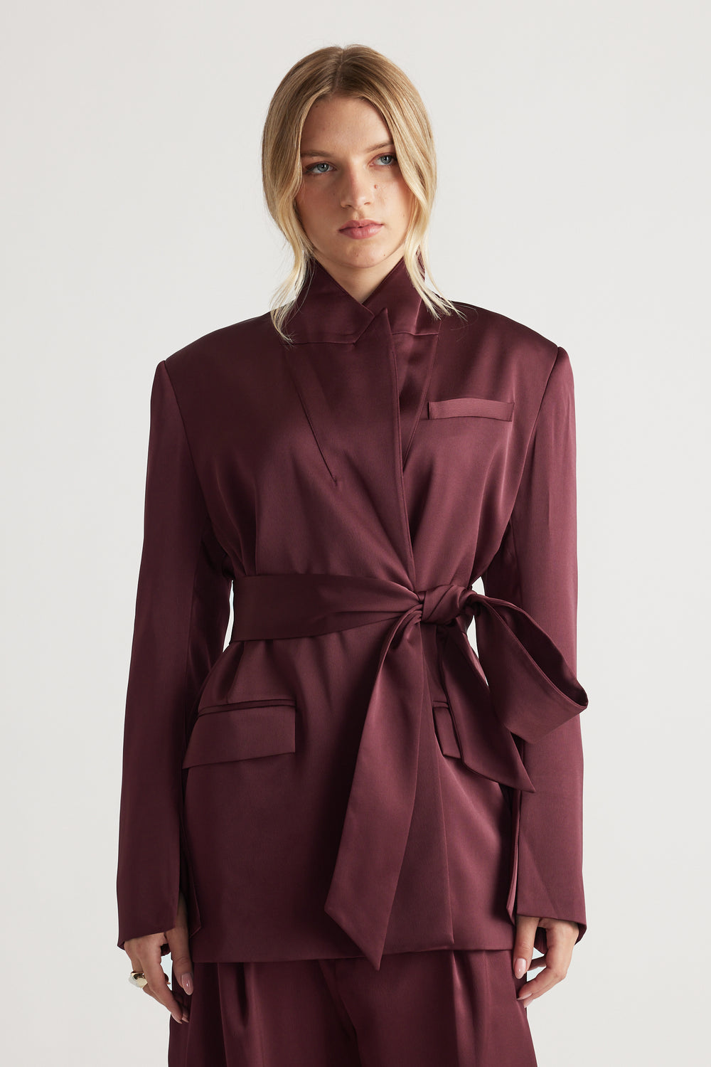 Woman wearing a deep plum satin wrap blazer with structured shoulders and a tied waist belt for a polished look