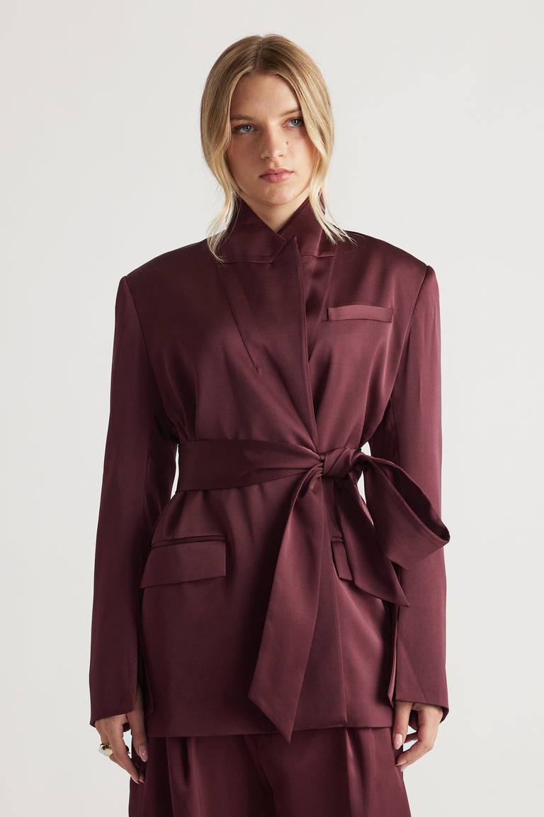 Woman wearing a deep plum satin wrap blazer with structured shoulders and a tied waist belt for a polished look