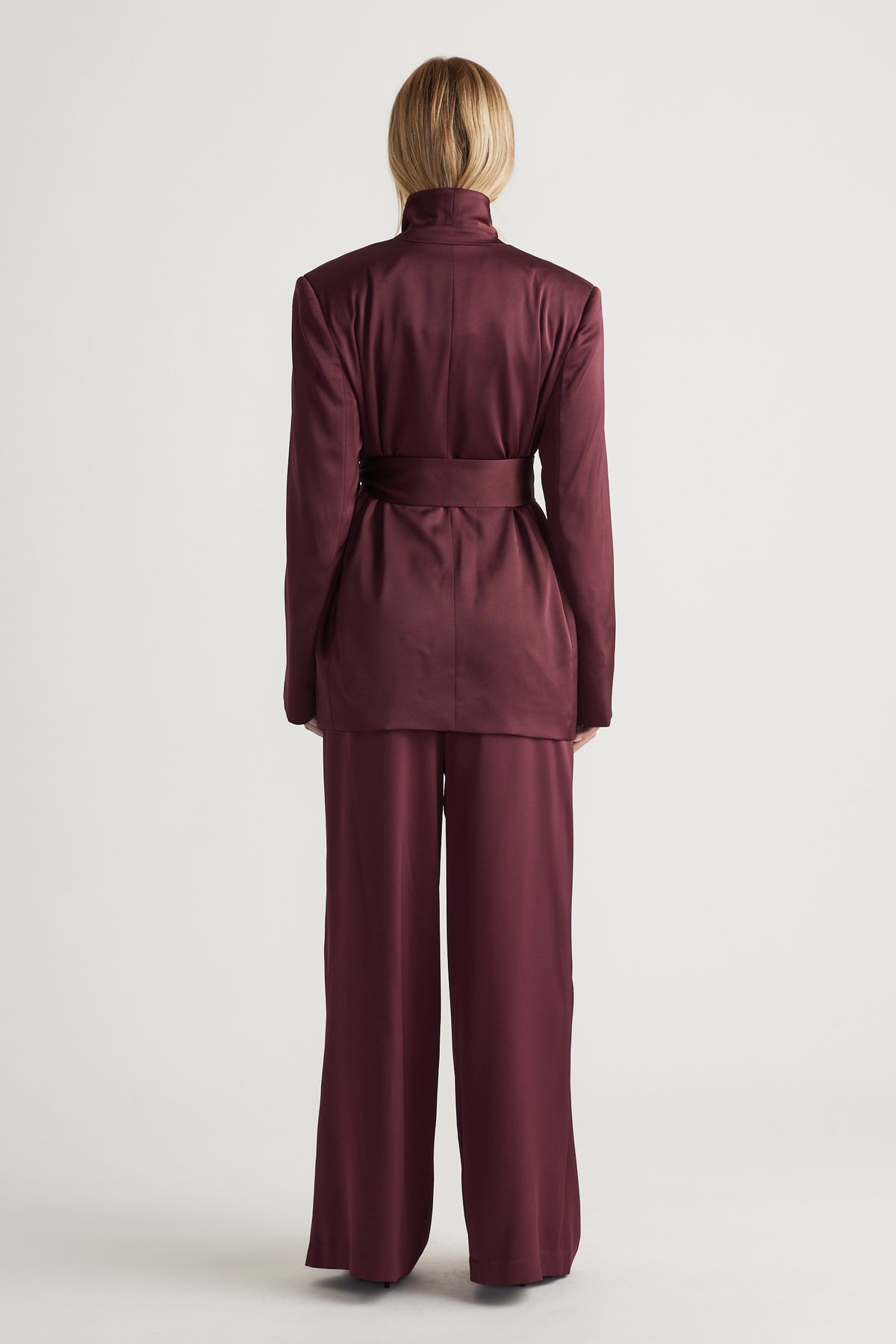 Back view of a woman wearing a plum satin wrap blazer with matching wide-leg trousers in a polished, modern look