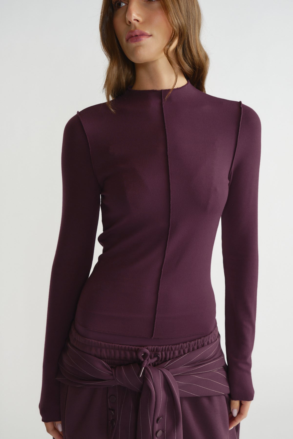 Woman wearing a fitted deep plum long sleeve top with a central seam detail, styled with matching waist-tied bottoms