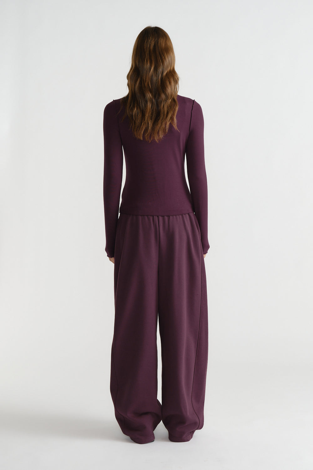 Back view of a woman wearing a fitted long sleeve top and relaxed wide-leg pants in deep berry tones