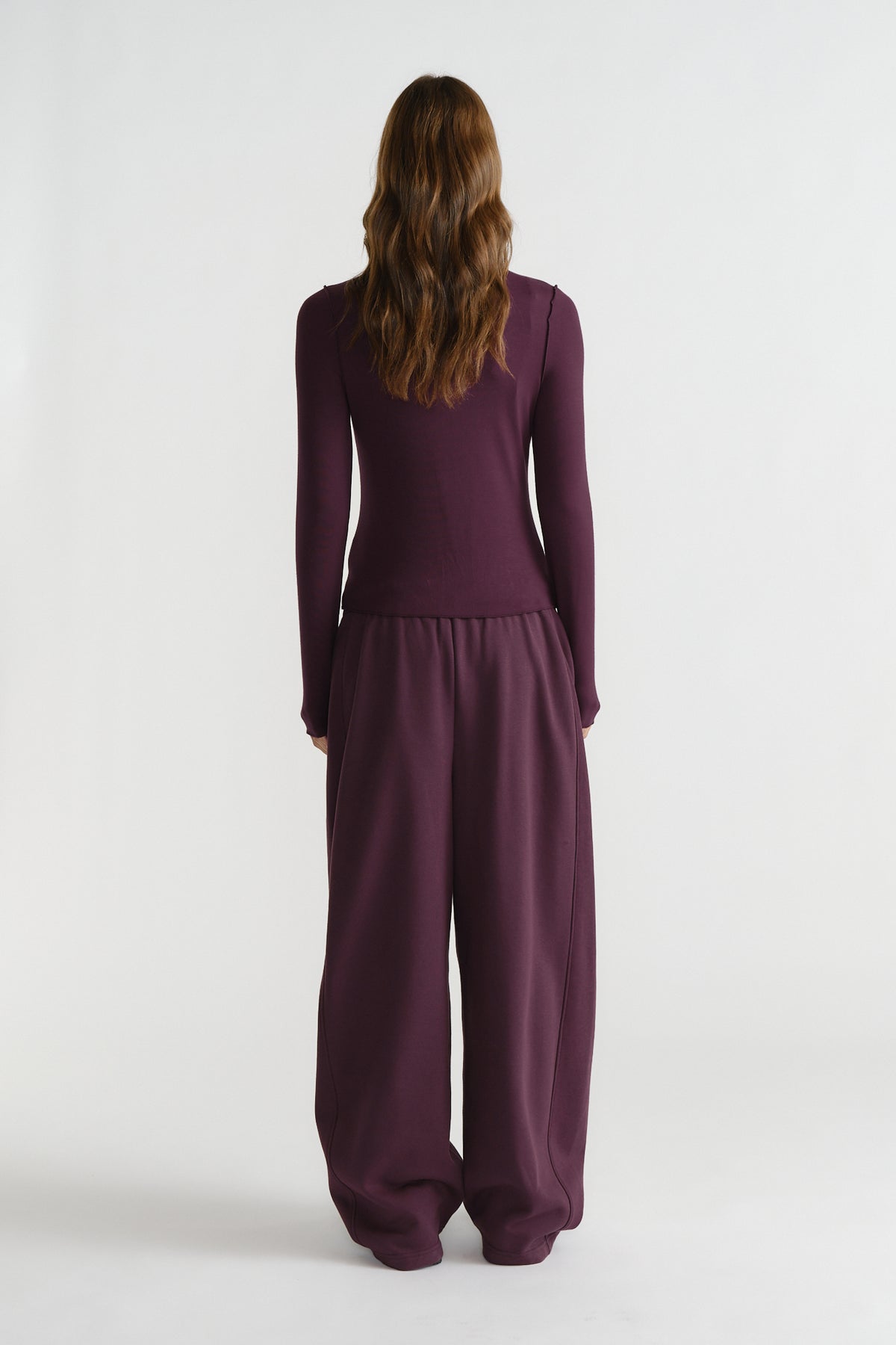 Back view of a woman wearing a fitted long sleeve top and relaxed wide-leg pants in deep berry tones