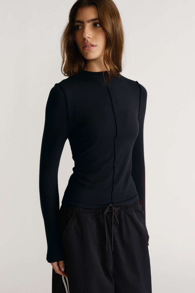 Woman wearing a navy fitted long sleeve top with a subtle centre seam detail and casual black drawstring pants