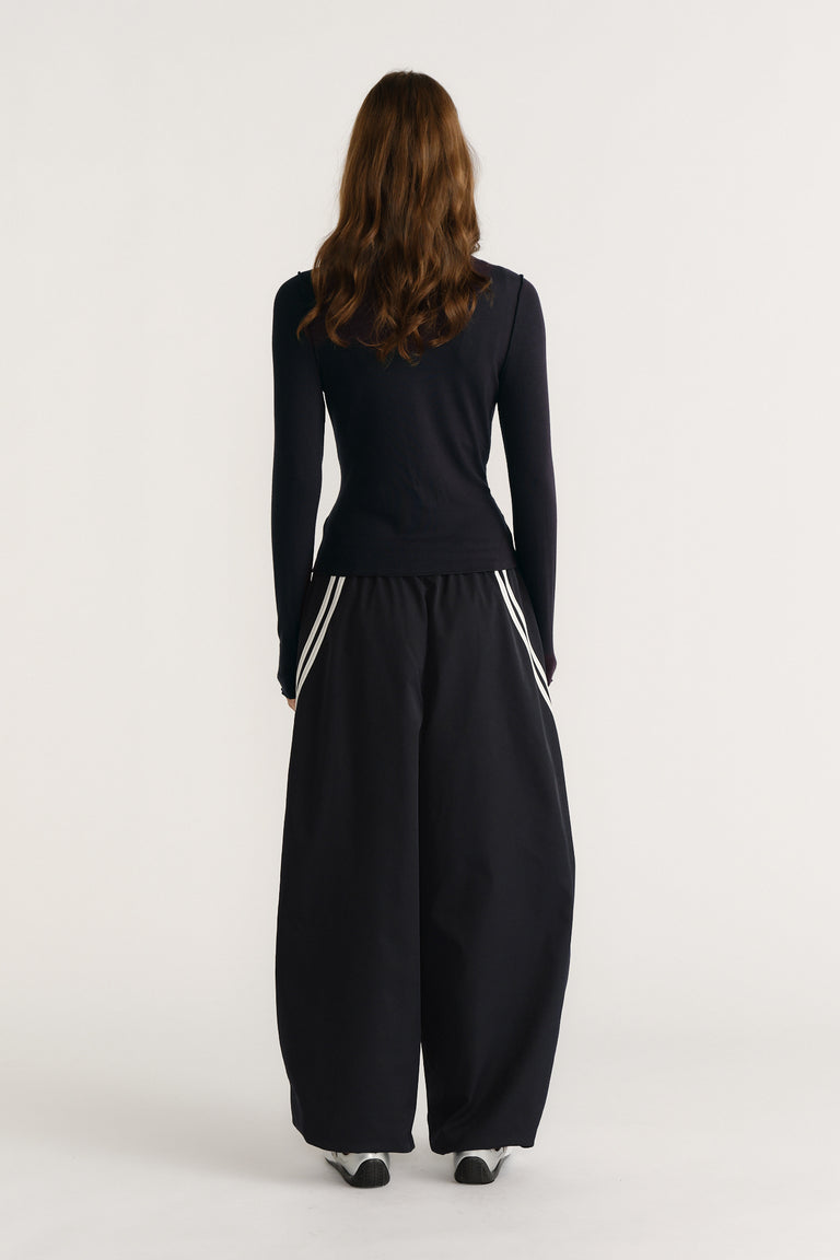 Woman wearing a navy long sleeve top paired with wide-leg black pants featuring white stripe pocket details