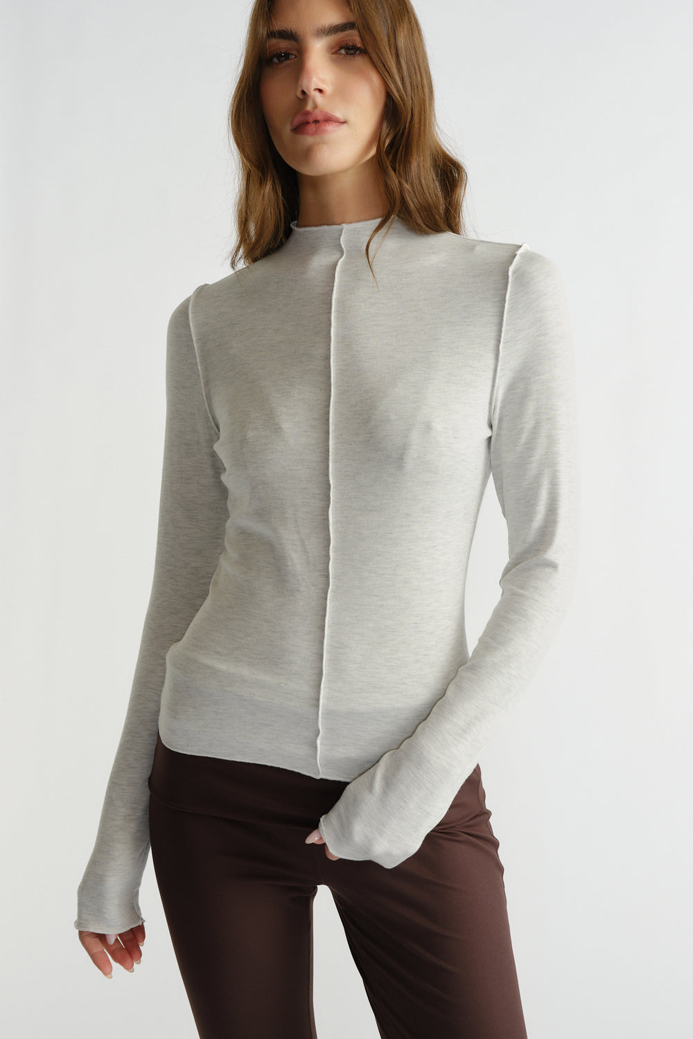 Woman wearing a fitted light grey long sleeve top with subtle seam detail, paired with dark brown pants.