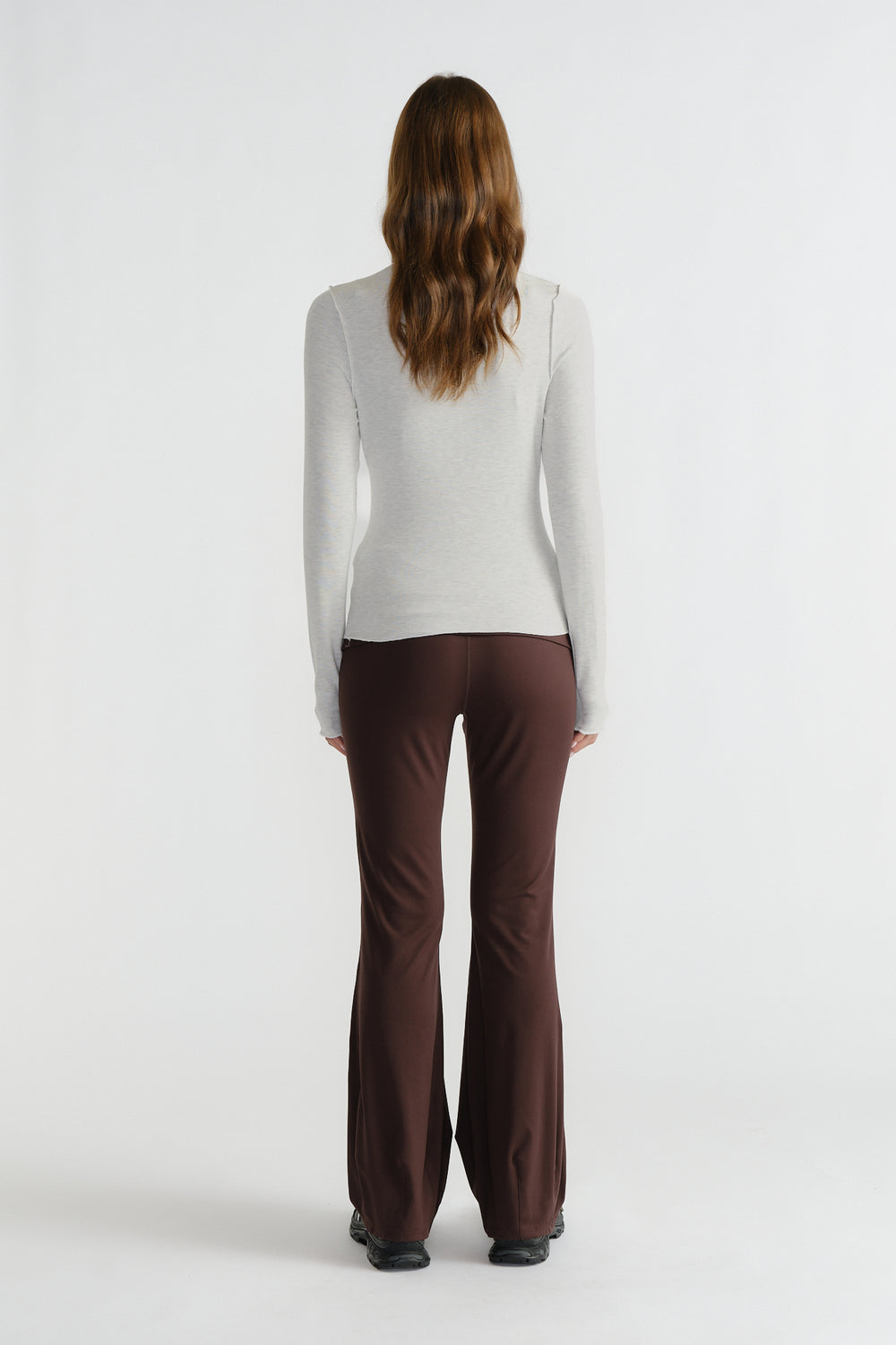Back view of woman wearing a fitted light grey long sleeve top paired with brown flared pants and black shoes.