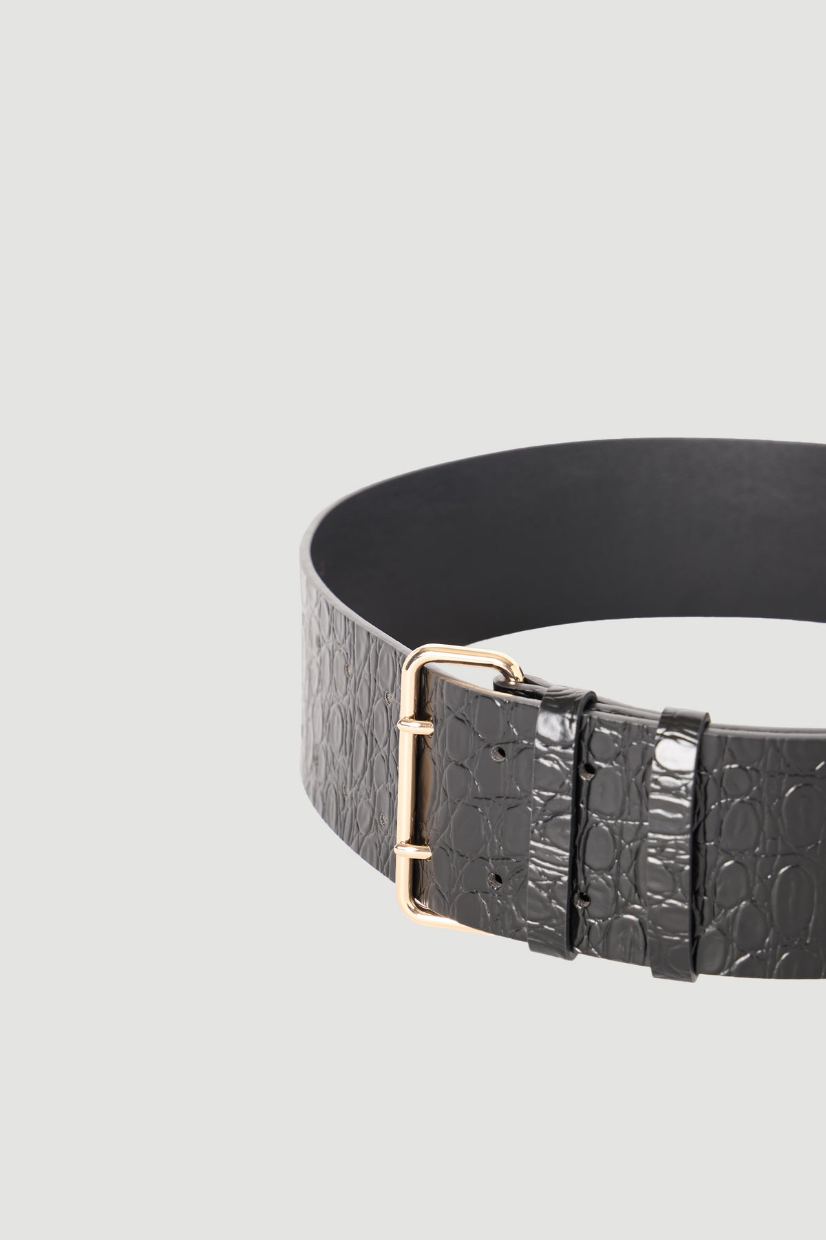 Close-up of a black wide belt with embossed texture and a polished gold-tone buckle against a neutral background