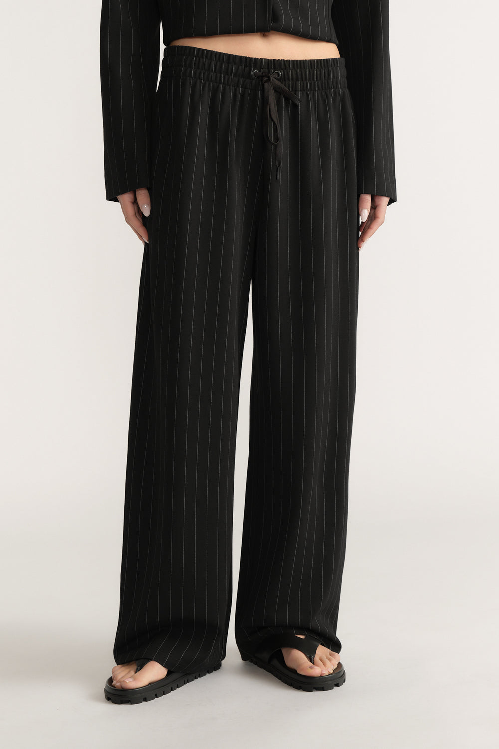Black wide-leg pants with white pinstripes, elasticated drawstring waist, and side pockets on model against plain background