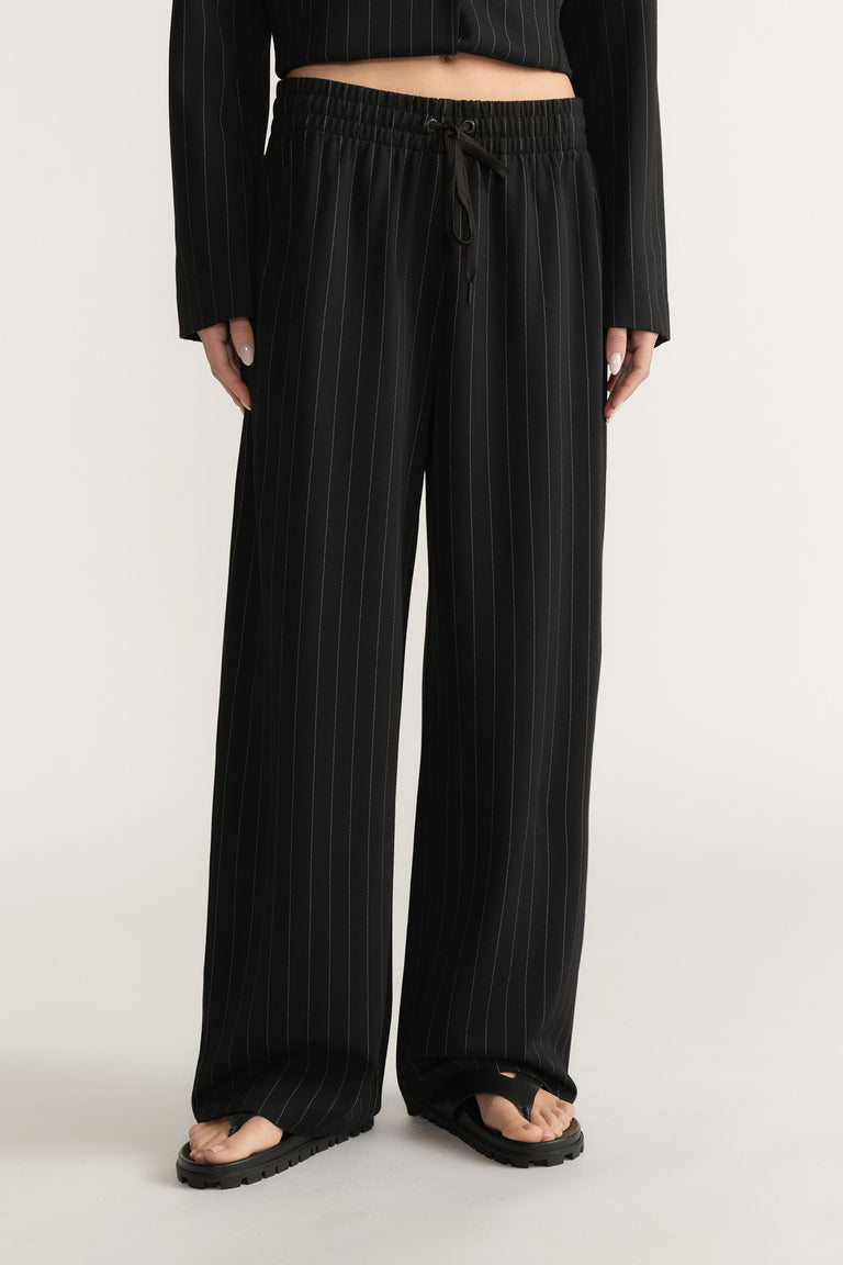 Black wide-leg pants with white pinstripes, elasticated drawstring waist, and side pockets on model against plain background