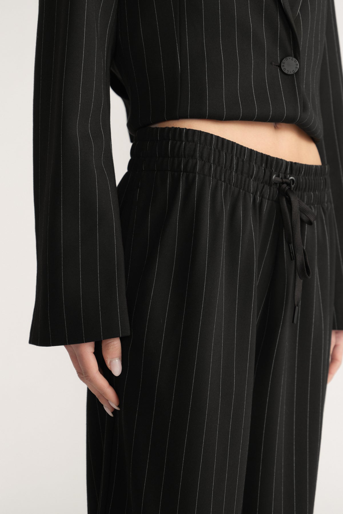 Close-up of black pinstripe wide-leg pants with elastic drawstring waist and side pockets worn with matching blazer