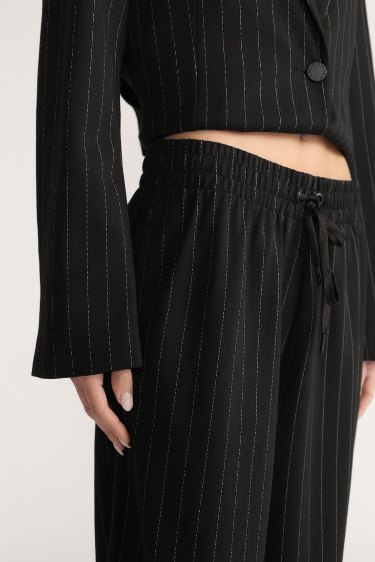 Close-up of black pinstripe wide-leg pants with elastic drawstring waist and side pockets worn with matching blazer