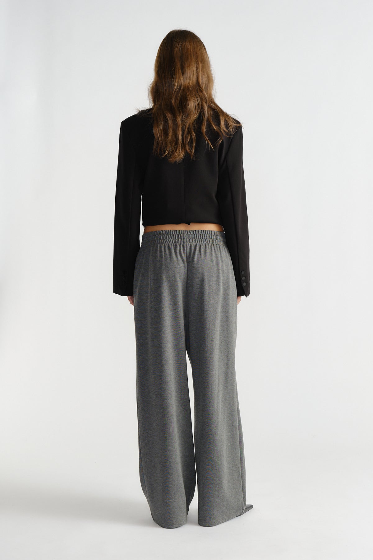 Back view of woman wearing relaxed fit charcoal pinstripe pants with elastic waistband and cropped black blazer.