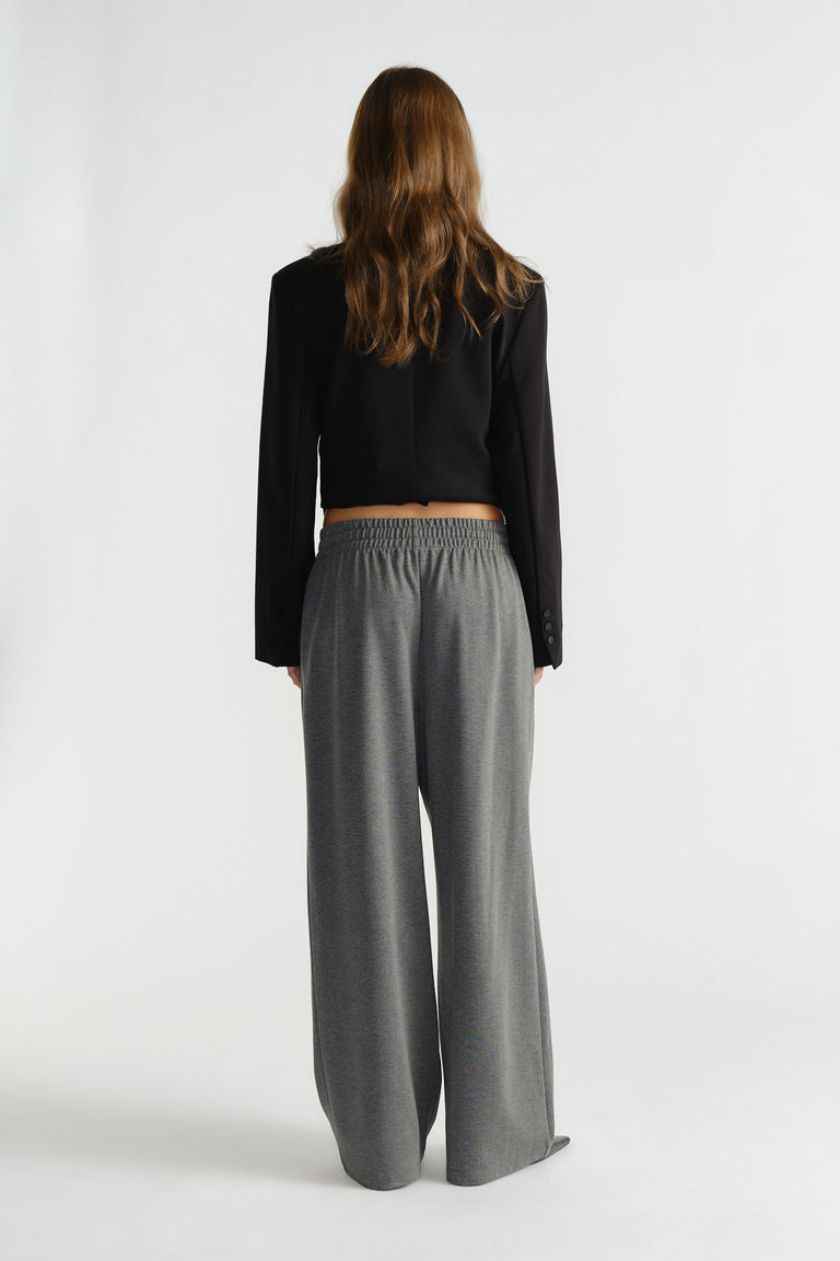 Back view of woman wearing relaxed fit charcoal pinstripe pants with elastic waistband and cropped black blazer.