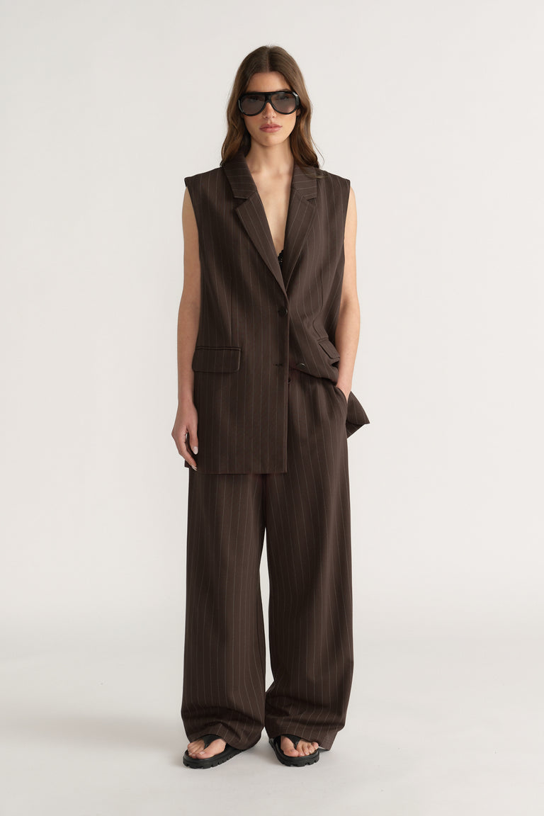 Woman wearing sleeveless brown pinstripe blazer and matching wide-leg pants with black sandals and sunglasses
