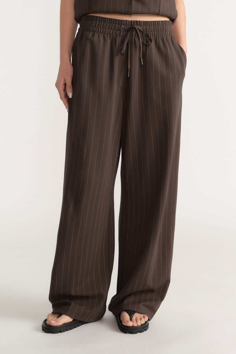 Wide-leg dark brown pants with white pinstripes, elasticated waist, drawstring, and side pockets worn with sandals