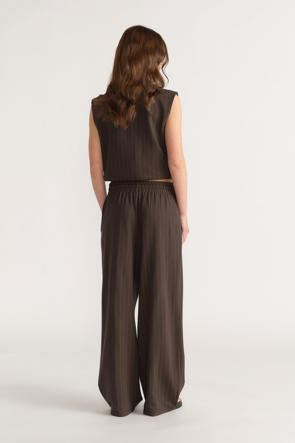 Woman wearing dark brown wide-leg pinstripe pants with elasticated waist and matching sleeveless top, back view