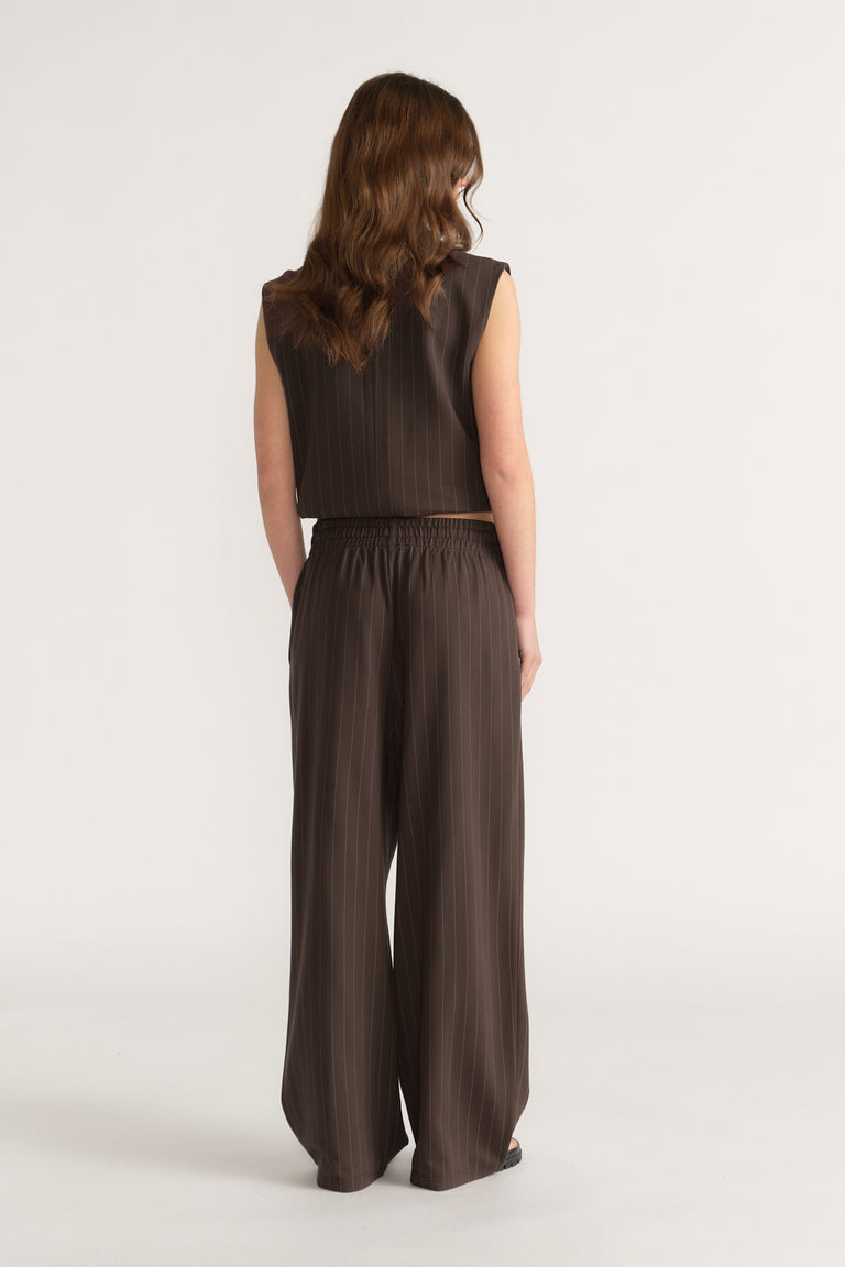 Woman wearing dark brown wide-leg pinstripe pants with elasticated waist and matching sleeveless top, back view